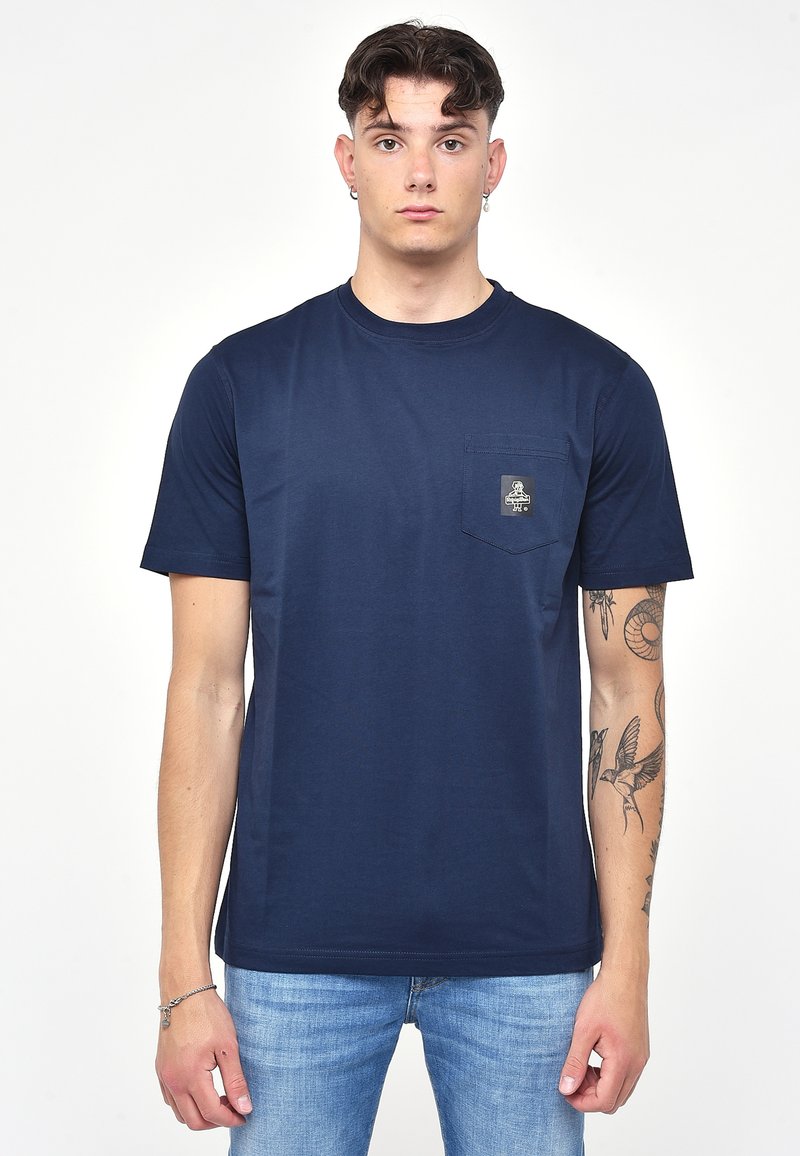 Mörkblå bomulls t-shirt med korta ärmar, rund nacke och en liten bröstficka med en liten logotyp. Bärs med ljusblå jeans.