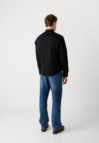Black long-sleeve shirt with a straight cut, paired with loose blue denim jeans. The jeans feature back pockets and a faded texture.