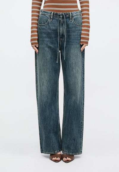 Calças de ganga de perna larga em azul desbotado, com cintura ajustável por cordão, cinco bolsos e bainha ligeiramente desfiada. Material com acabamento texturizado.