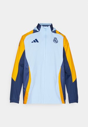 Chaqueta de cremallera azul claro con acentos amarillos y marino, que presenta el logo de Adidas y el emblema del Real Madrid en el pecho. Tejido ligero.