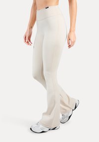 Lichtbeige wijde broek gemaakt van stretchstof, met een hoge tailleband en naadloos ontwerp, gecombineerd met witte sportschoenen.