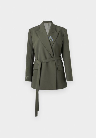 Blazer verde oliva con una vestibilità sartoriale, colletto a revers e vita cinturata. Presenta ricami floreali sulla manica sinistra e tasche laterali.