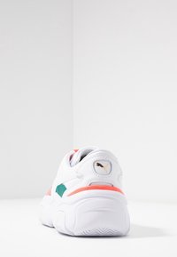 Weißer Sportschuh mit pinken Akzenten, tealfarbenem Seitenteil, runder Form und strukturiertem Sohlenprofil. PUMA-Logo auf der Ferseneinlage, aus synthetischem Material.