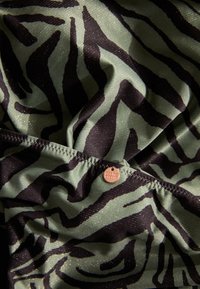 Zebra-print stof met zwarte en olijfgroene strepen en glinsterende accenten; inclusief een klein merklabel dat in de zoom is gestikt.