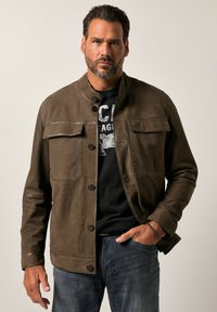 Bruine leren jas met een staande kraag, twee borstzakken en knoopsluiting. Draag over een zwart shirt, gecombineerd met donkere jeans.