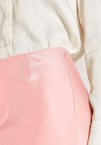 Lichtroze satijnen rok met een aansluitende taille, zijritssluiting en een soepele textuur, gecombineerd met een crème blouse met knopen.