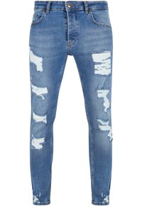 Jeans ajustados de color azul claro, confeccionados en denim, con múltiples desgastes y desgarros, una cinturilla estándar y bordes deshilachados en las áreas rasgadas.
