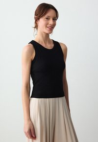 Top senza maniche nero a costine con scollatura rotonda, abbinato a una gonna plissettata fluida di colore chiaro, con una texture liscia.