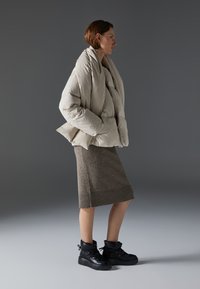 Giacca beige voluminoso con colletto alto, sovrapposta a una gonna a maglia marrone. Scarpe high-top in platform nere con lacci e cinghie.