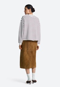 Felpa a righe bianca e bordeaux con spalle scese abbinata a una gonna in pelle scamosciata marrone di media lunghezza e calzini bianchi alla caviglia.