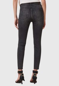 Vaqueros skinny negros con un ligero desgaste, con dos bolsillos traseros y un dobladillo sin terminar. Se llevan con zapatos de tacón alto negros con correas en los tobillos.