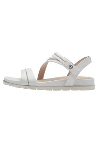 Vit sandal med tvärgående remmar och spänne på sidan. Gummisula, platt design, lätt klack och subtil metallisk detalj på remmen.