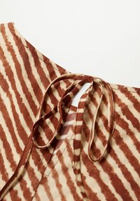 Hnědo-krémová látka s vzorem, se zavazováním, zdobená vlnitými pruhy a výstřihem do lodičky. Měkká textura a hladký povrch.