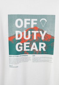 Vit t-shirt med "OFF DUTY GEAR" i fet grön och vit text, med grafiken av ett rött berg. Texten nedanför beskriver militära fallskärmshoppprocedurer.