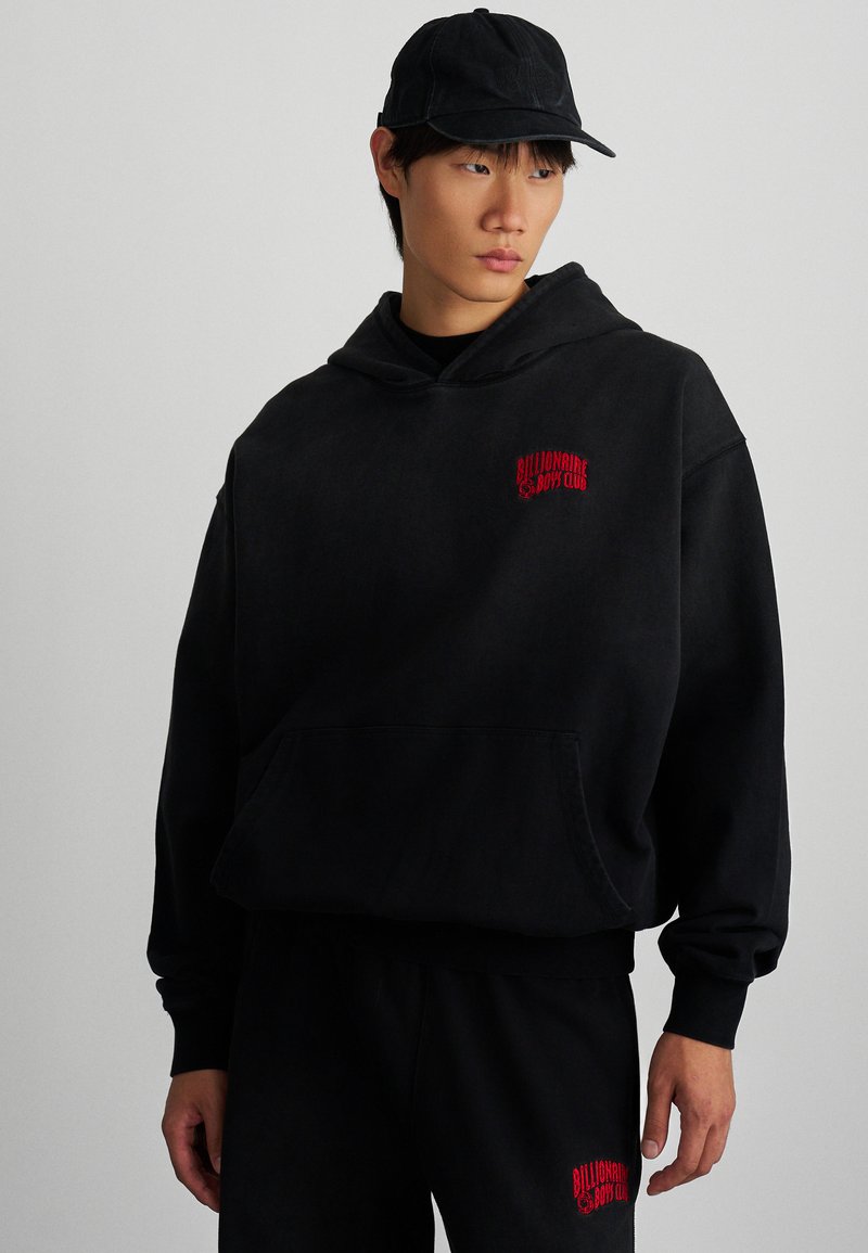 Sudadera negra de tejido suave, con un logo rojo de "Billionaire Boy Club" en el pecho, un bolsillo frontal y un corte holgado para mayor comodidad.