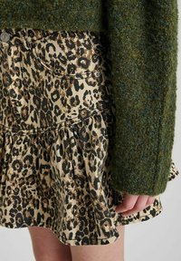 Denim rok met luipaardprint en een uitlopende onderrand, gecombineerd met een donkergroene textuurtrui, die de contrasten in stof en printdetails laat zien.