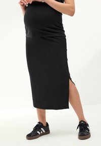 Schwarzes geripptes Kleid mit einem seitlichen Schlitz, weicher Textur und tailliertem Design, kombiniert mit schwarzen Sneakers mit weißen Streifen und einer braunen Sohle.