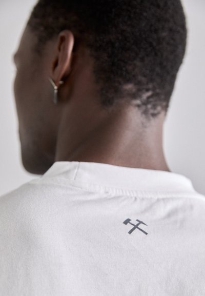 Weißes Baumwoll-T-Shirt mit einem kleinen grauen Grafikdesign auf der Rückseite und einem einfachen Rundhalsausschnitt. Glatte Textur mit sauberen Nahtdetails.