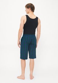Débardeur noir et shorts à carreaux en bleu, vert et noir. Les shorts disposent d'une taille élastique et arrivent juste au-dessus du genou.