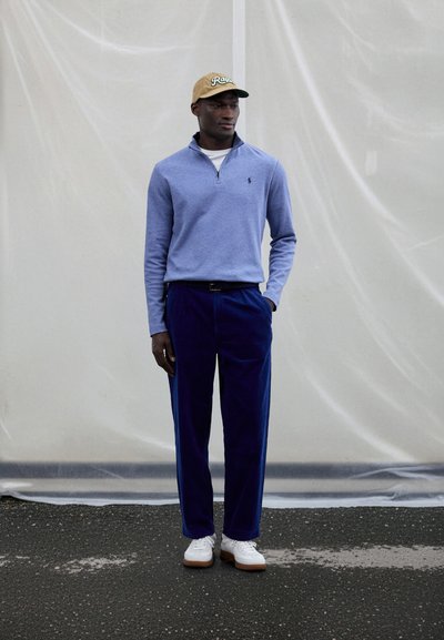 Gaiši zils puszipa džemperis, tumši zili kordbikses un baltas kedas. Bēša cepure ar zaļiem burtiem. Vienkāršas, tīras līnijas un faktūras.