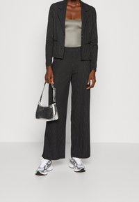 Osoba v černém pruhovaném blejzru a kalhotách, šedém topu, bílých teniskách a držící malou stříbrnou kabelku.