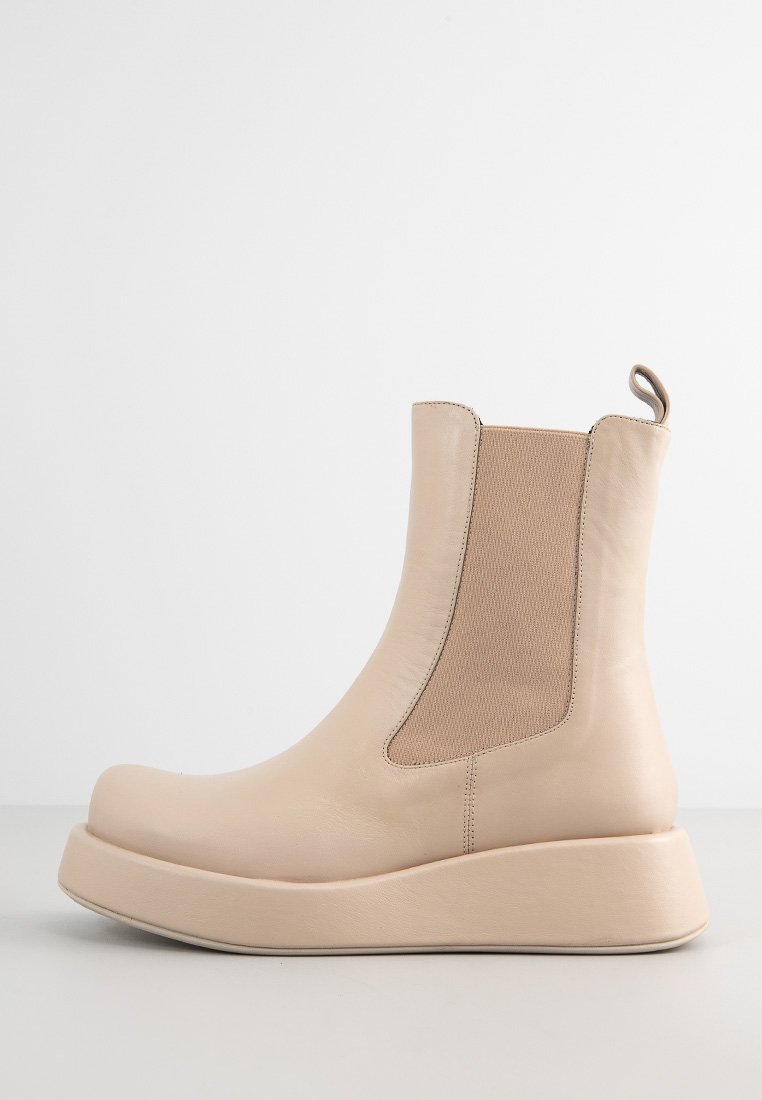 Botines beige con cuero suave, paneles laterales elásticos, punta redondeada y suela gruesa y acolchada. Diseño minimalista con una lengüeta.