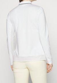 Biała koszula z długim rękawem, z teksturowaną siateczkową wstawką po bokach i jednolitym tyłem, z kołnierzykiem i kontrastowym wykończeniem wzdłuż dekoltu.