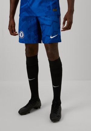 Blå fodboldshorts med geometrisk mønster, Chelsea FC-logo og Nike-emblem. Kombineret med sorte knæhøje sokker og sorte fodboldstøvler.