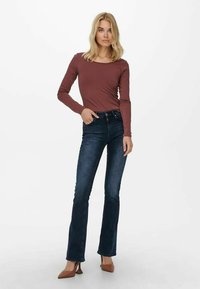 Maglietta a maniche lunghe color bordeaux abbinata a jeans a zampa d'elefante blu scuro e scarpe con tacco marroni, per un look casual e aderente.