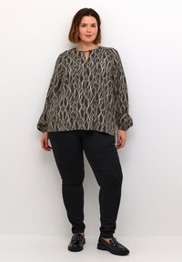 Svart och beige mönstrad blus med rund halsringning, kort nyckelhål och puffärmar, i kombination med åtsittande svarta byxor och skor.