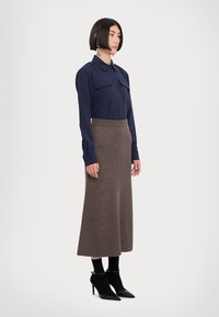 Marineblå skjorte med knapper og to brystlommer, parret med en brun ribbet lang nederdel. Modellen har sorte hæle og strømper på. Enkel design.
