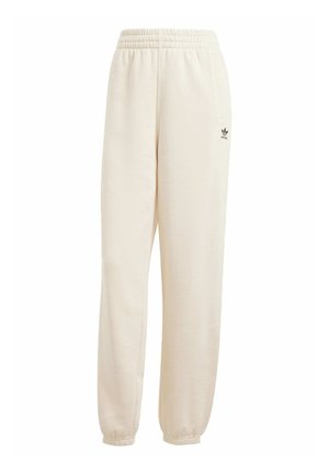Pantalon de survêtement beige avec taille élastique, chevilles resserrées et un petit logo Adidas noir sur la jambe gauche. Fabriqué en tissu doux et texturé.