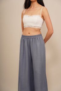 Un top court blanc avec des bordures en dentelle et des fines bretelles, associé à un pantalon large loose de couleur bleu clair avec une taille élastique.