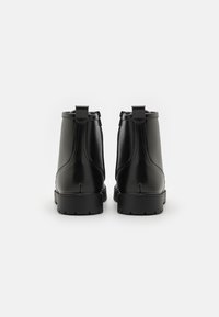 Černé kožené kotníkové boty s hladkým povrchem, minimálním prošíváním, prodlouženým tvarem a malými poutky na patě.