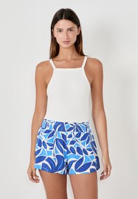 Débardeur blanc à côtes avec des bretelles étroites, associé à un short bleu décoré d'un motif de feuilles dans des nuances de bleu et de blanc.