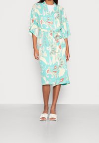 Lekki, turkusowy kimono w kwiatowe wzory, z krótkimi rękawami i paskiem w talii. W połączeniu z białymi klapkami na płaskim obcasie.