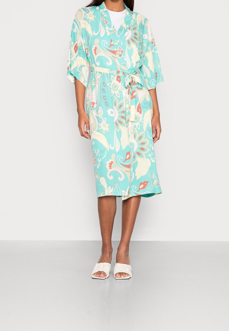 Lekki, turkusowy kimono w kwiatowe wzory, z krótkimi rękawami i paskiem w talii. W połączeniu z białymi klapkami na płaskim obcasie.