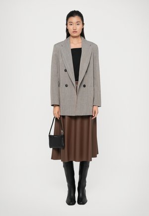 Double-breasted gray blazer over a black top, brown pleated skirt, black knee-high boots, and a small black handbag. Smooth fabric textures.