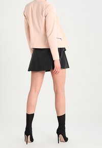 Ljust rosa skräddarsydd jacka med en slät textur, kombinerad med en svart fusk läderkjol och svarta högklackade strumpstövlar.