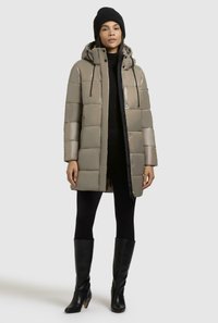 Giacca imbottita in grigio chiaro con finitura lucida, dotata di cappuccio, bottoni a pressione e silhouette dritta. Abbinata a leggings neri e stivali al ginocchio.