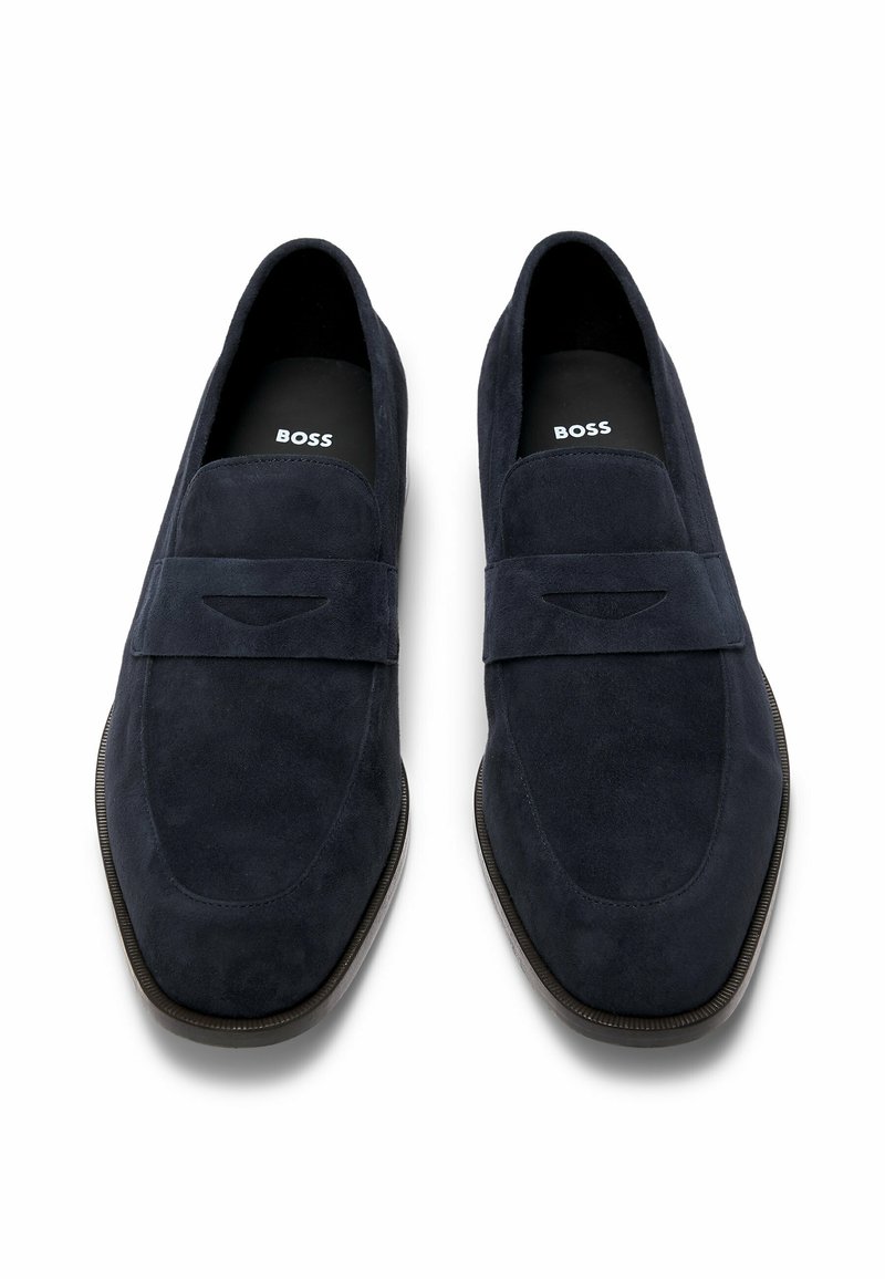 Mocassins en daim bleu marine à finition lisse, avec une bandoulière décorative et un subtil détail découpé. Logo noir sur la semelle intérieure.