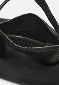 Sac en cuir noir avec une texture lisse, doté d'une grande ouverture zippée et de poches intérieures, y compris un petit compartiment zippé.