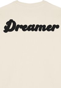 Felpa crema con grande scritta ricamata in nero "Dreamer" sul retro. Collo rotondo con bordo a costine. Materiale in cotone morbido.