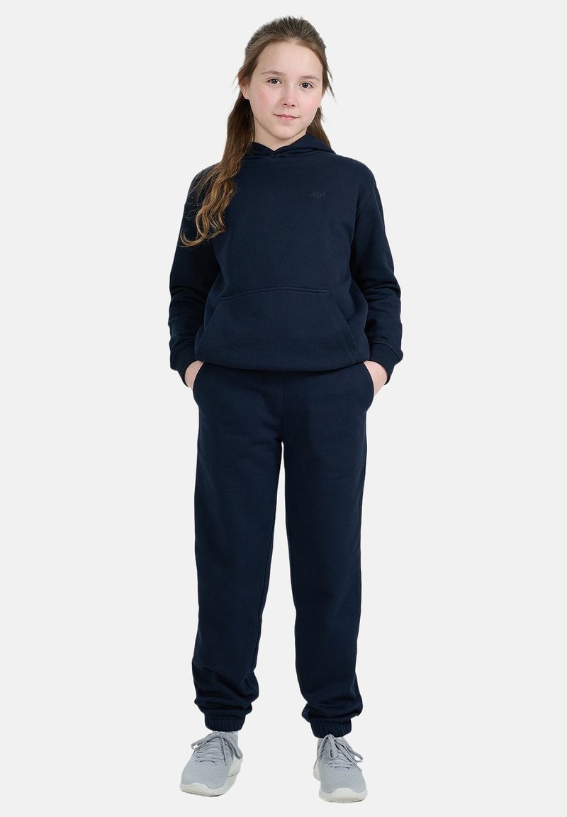 Sweat à capuche bleu marine et joggings assortis en tissu doux, avec une poche avant et des poignets élastiques, associés à des baskets gris clair.