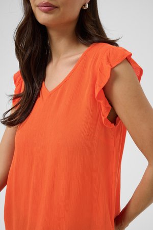 Femme portant un haut orange vif sans manches avec des détails à volants aux épaules et un décolleté en V, montrant une partie de son visage et de longs cheveux foncés.