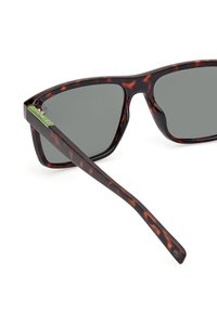 Brązowe okulary przeciwsłoneczne w kratkę z szarymi soczewkami, z gładkim, błyszczącym wykończeniem i zielonym akcentem na zausznikach.