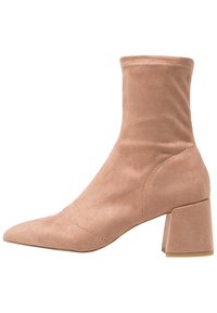 Bottines en daim rose clair avec un bout pointu et un talon carré épais. Présentent un design sans couture et des détails de couture minimalistes.