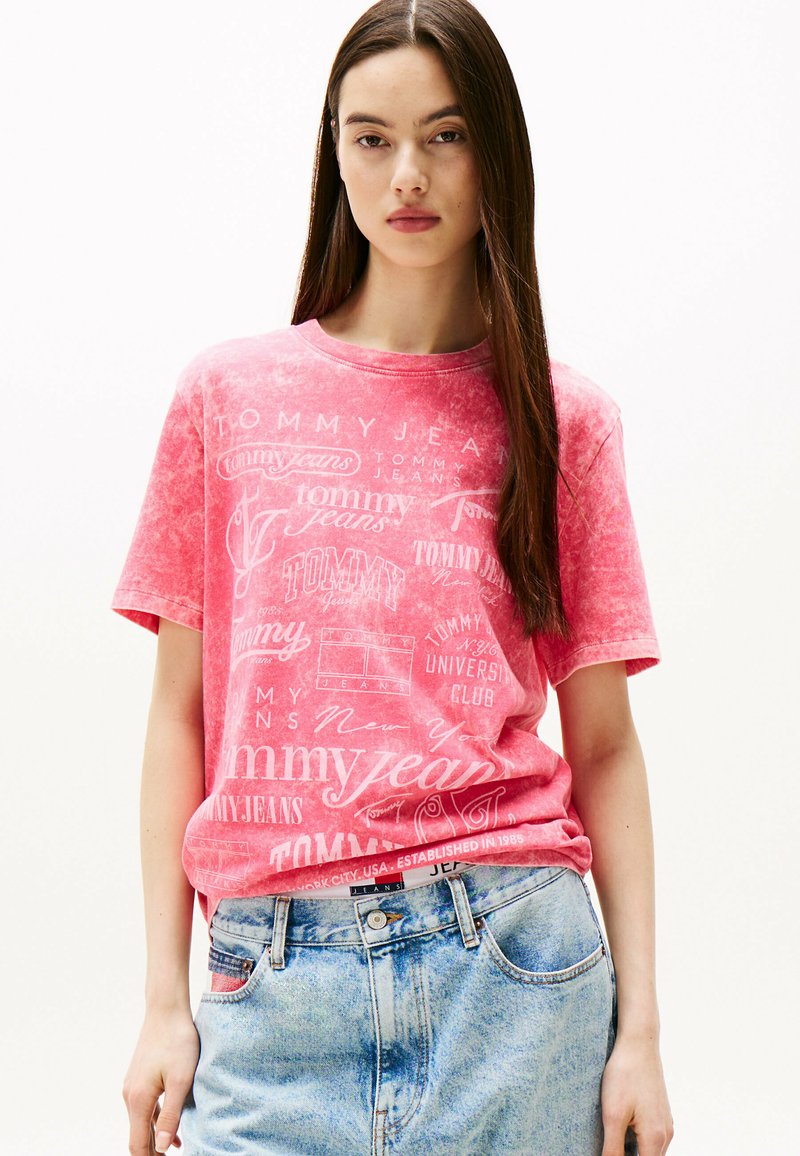 Różowa bawełniana koszulka z okrągłym dekoltem i krótkimi rękawami, z luźnym krojem, ozdobiona białymi nadrukowanymi logo i tekstem, połączona z szortami dżinsowymi z wysokim stanem.