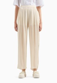 Pantaloni a palazzo plissettati in tessuto beige chiaro, con vita alta e spacchi laterali, abbinati a sneaker beige in piattaforma texturizzate.