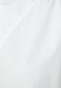 Tessuto bianco con finitura opaca, caratterizzato da una cucitura diagonale che crea texture visive e profondità. Materiale liscio e leggero.